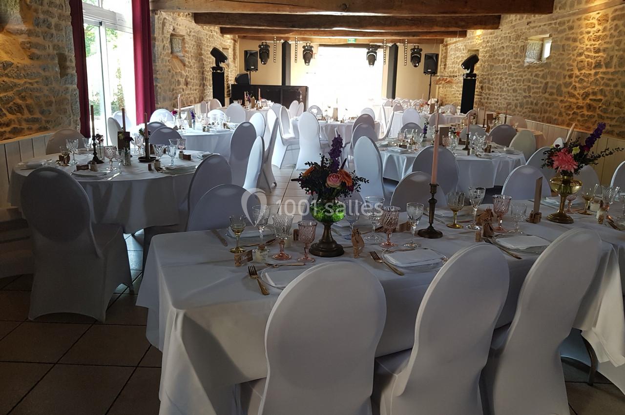Salle de réception décorée pour un événement, avec des tables dressées, nappes blanches et arrangements floraux.