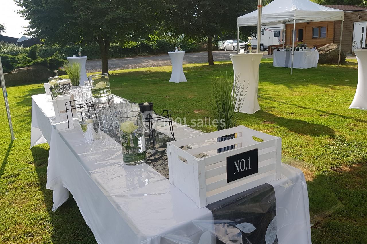Table décorée en extérieur sous une tente, avec des éléments en verre, des plantes et une caisse en bois blanche.
