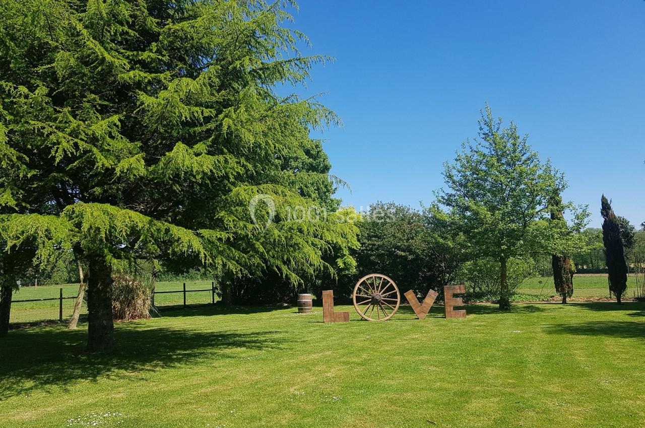 Grand jardin verdoyant avec des arbres, une roue en bois et des lettres formant le mot ’LOVE’ sur l'herbe.
