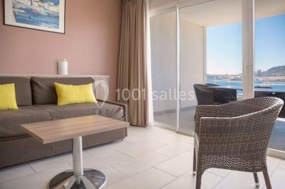 Ordinateur portable ouvert sur une table blanche avec carnet, tasse de café et plantes suspendues au-dessus.