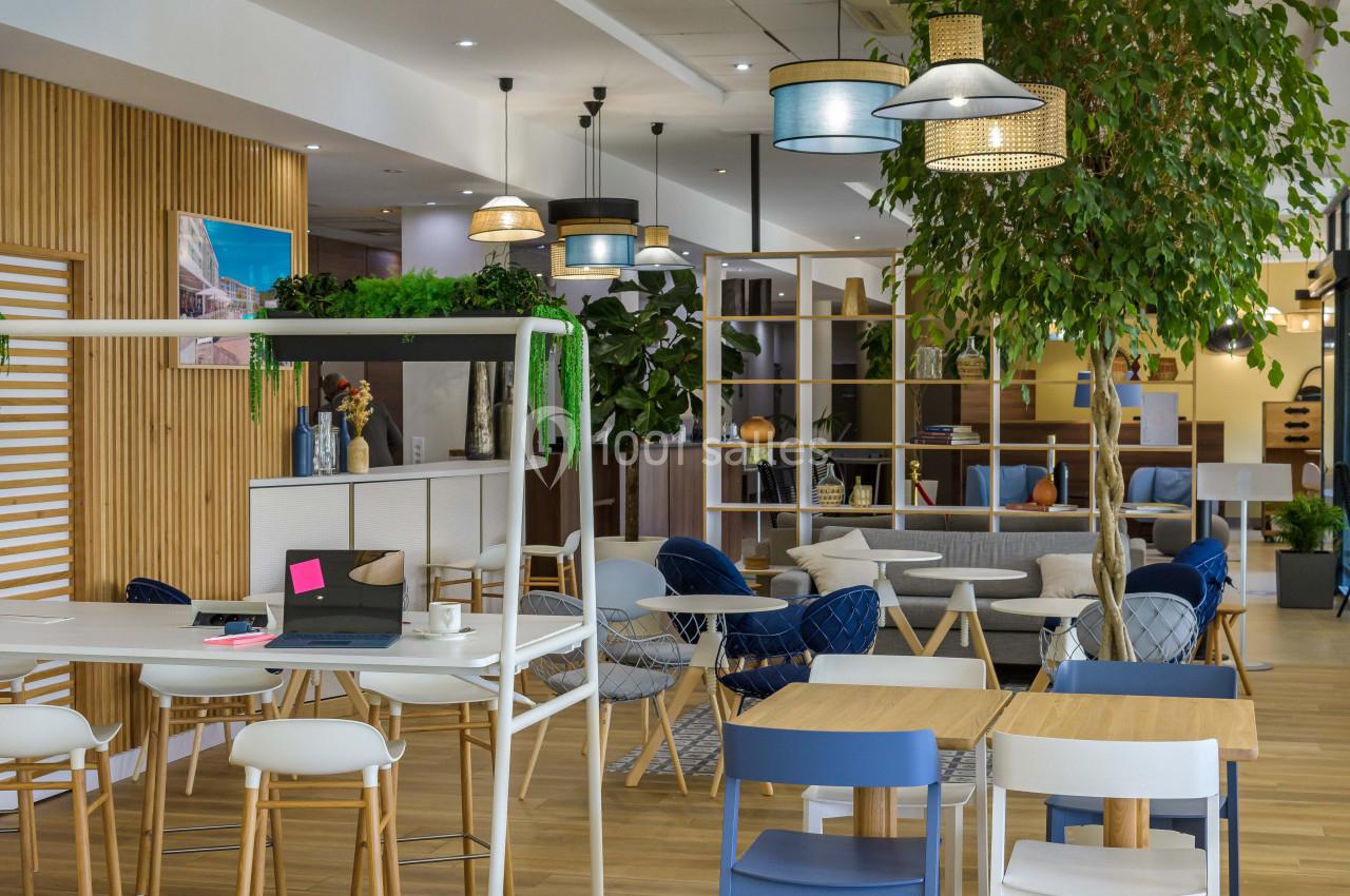 Espace intérieur moderne avec mobilier varié, plantes et éclairage suspendu, conçu pour le travail ou la détente.