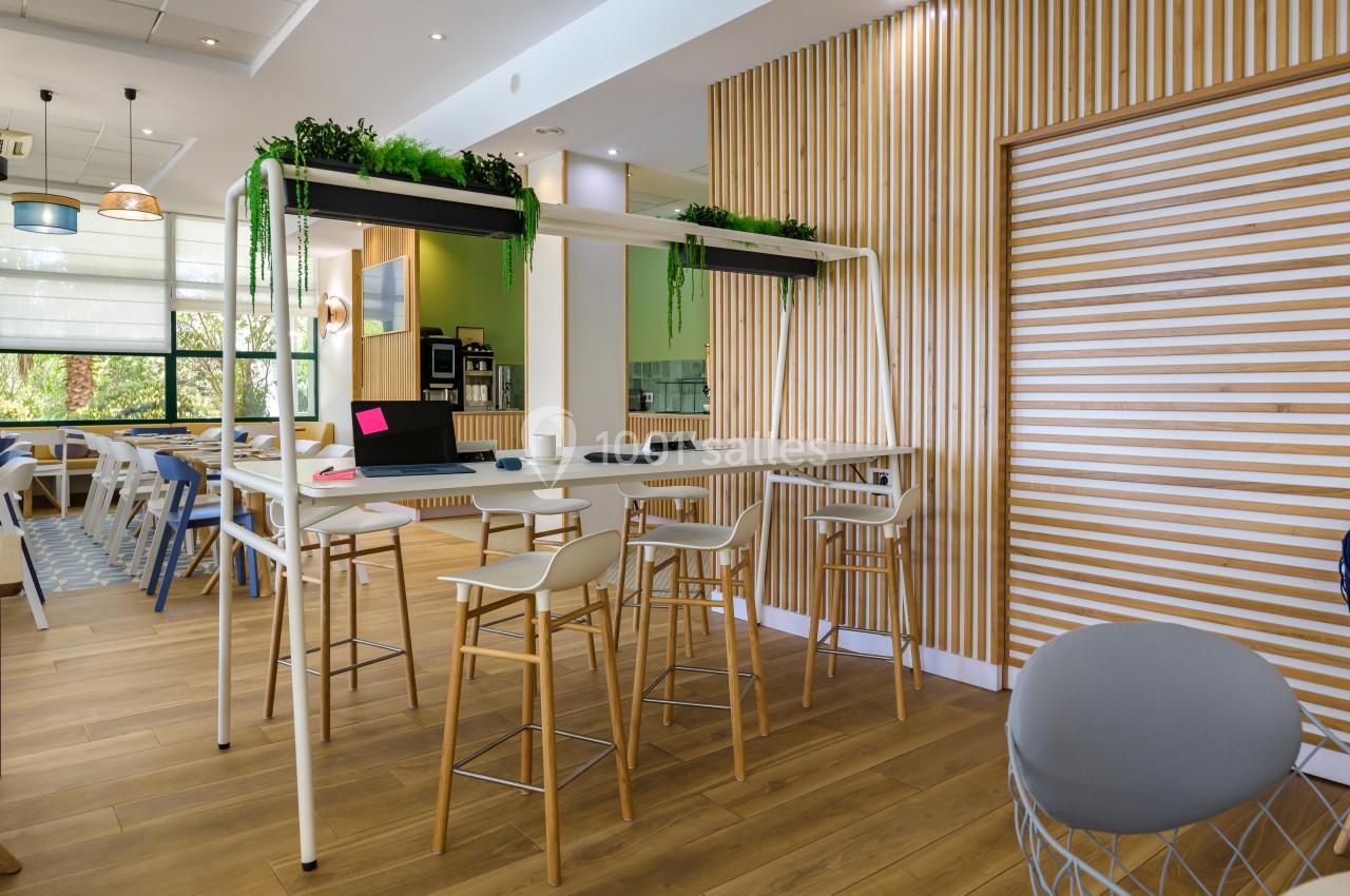 Espace de coworking lumineux avec table haute, chaises modernes, plantes décoratives et parquet en bois clair.