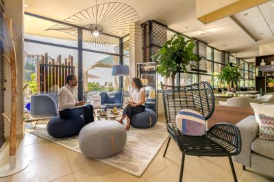 Ordinateur portable ouvert sur une table blanche avec carnet, tasse de café et plantes suspendues au-dessus.