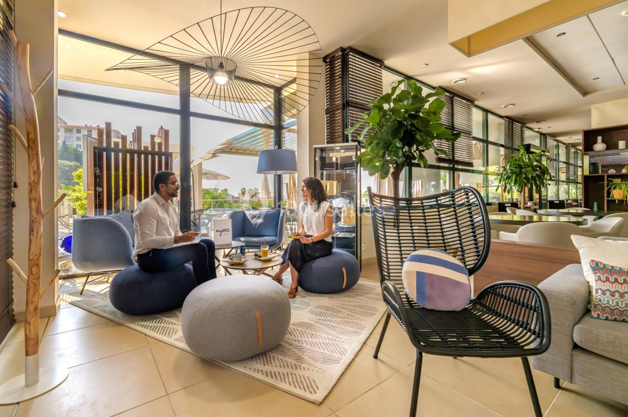 Deux personnes discutent dans un salon moderne et lumineux, entourées de meubles design et de plantes.