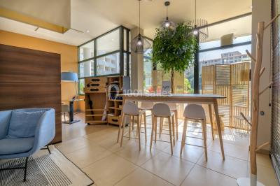 Ordinateur portable ouvert sur une table blanche avec carnet, tasse de café et plantes suspendues au-dessus.