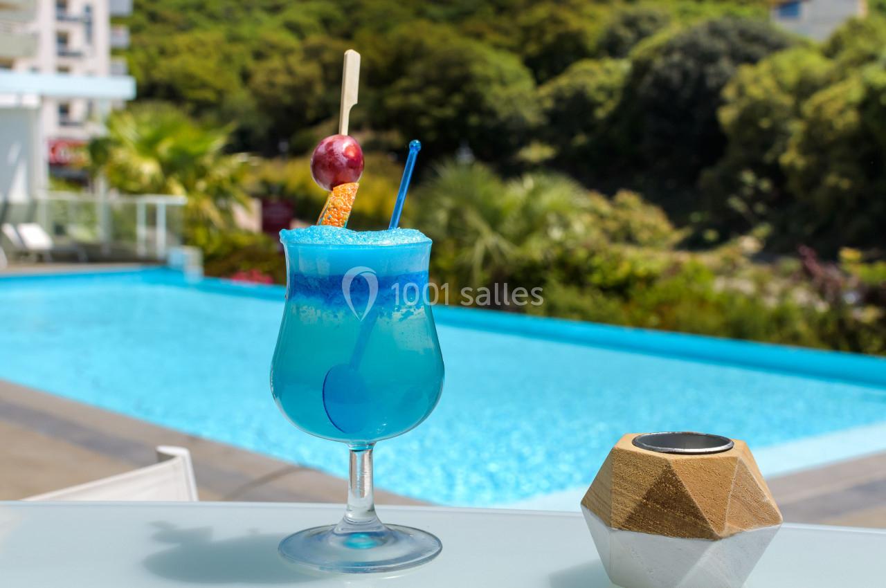 Cocktail bleu décoré d'une cerise et d'une rondelle d'orange, posé sur une table près d'une piscine extérieure.
