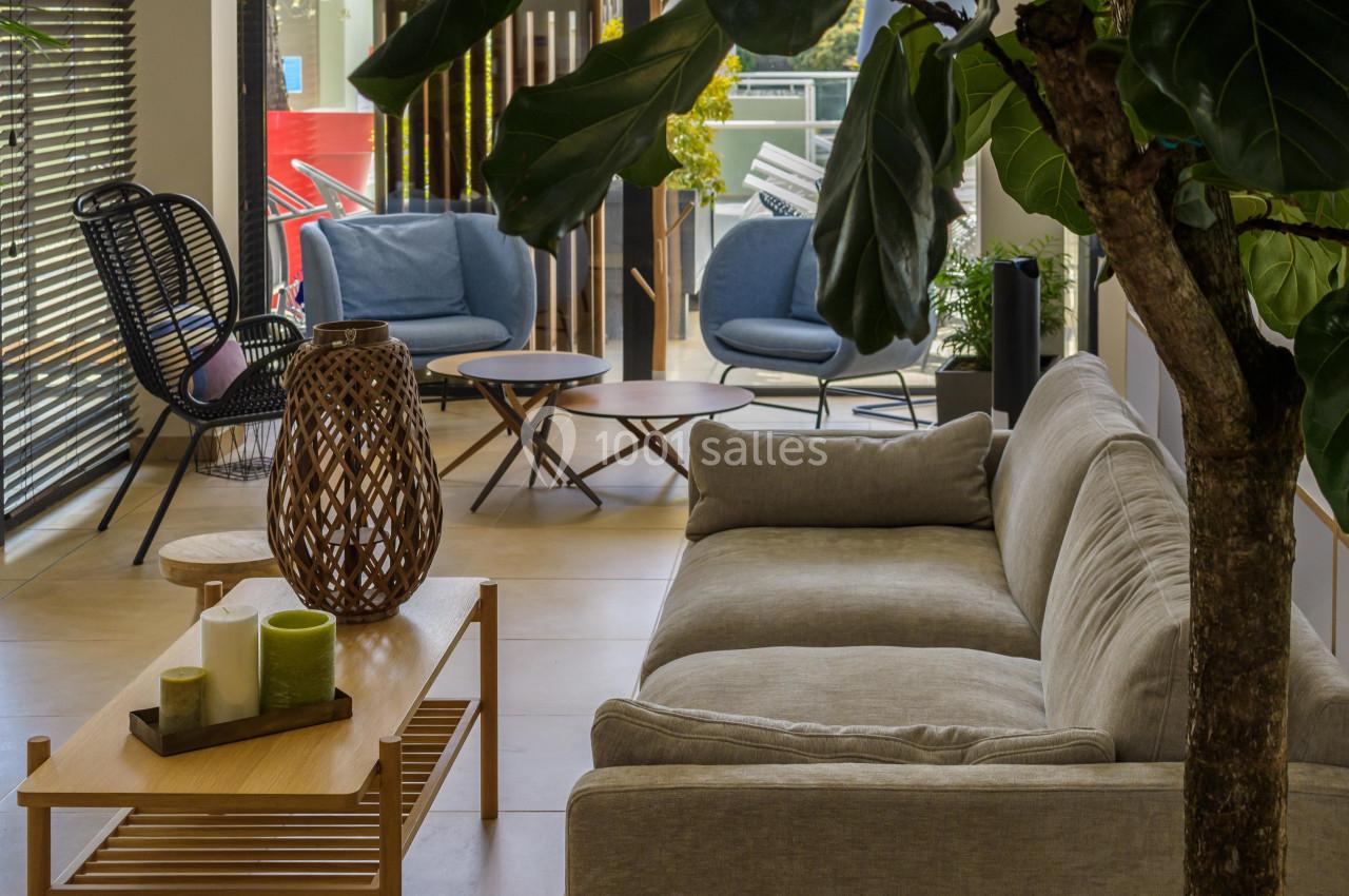 Espace salon moderne avec canapé beige, fauteuils bleus, table basse en bois et plantes décoratives.