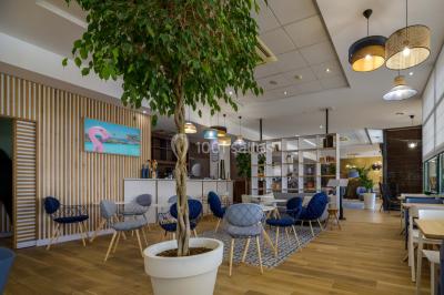 Ordinateur portable ouvert sur une table blanche avec carnet, tasse de café et plantes suspendues au-dessus.