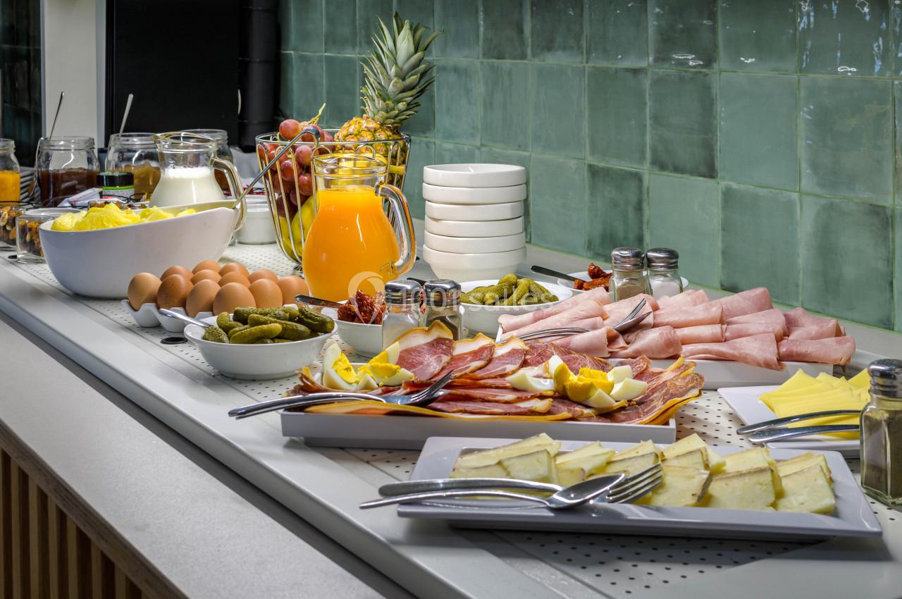 Buffet avec charcuterie, œufs, fromage, cornichons, jus d'orange et fruits, disposés sur un comptoir carrelé vert.