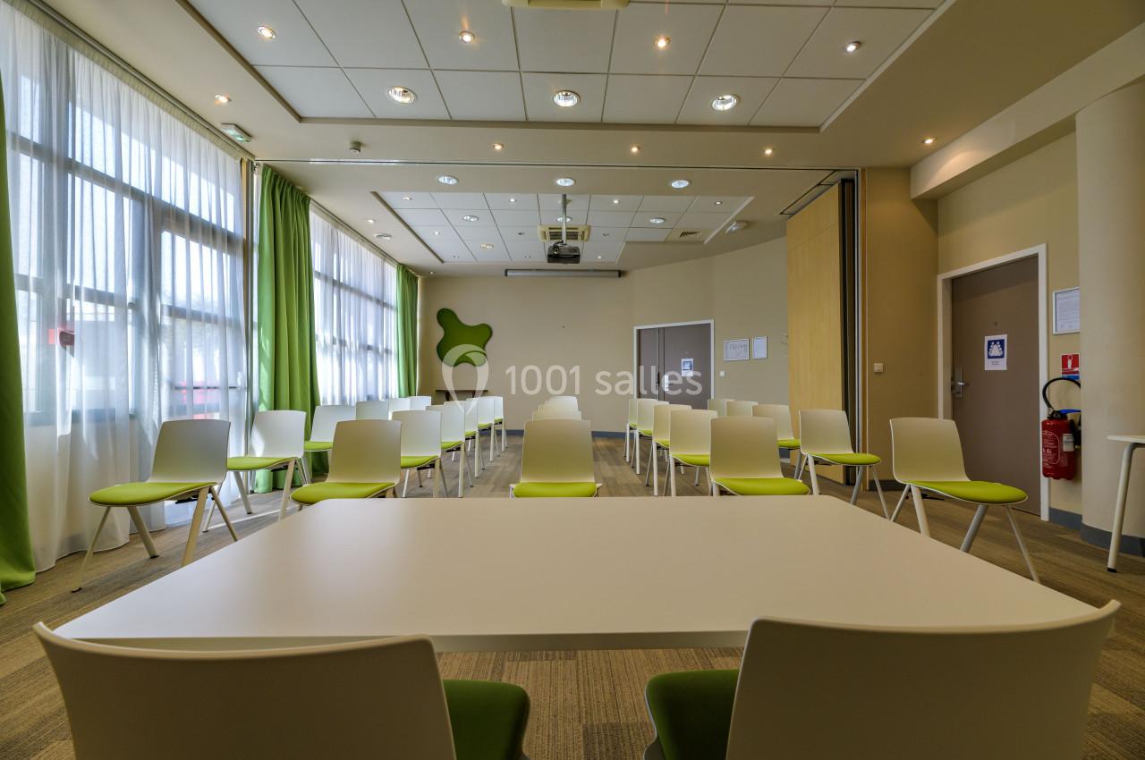 Salle de réunion lumineuse avec des chaises blanches et vertes, tables blanches et grandes fenêtres avec rideaux verts.