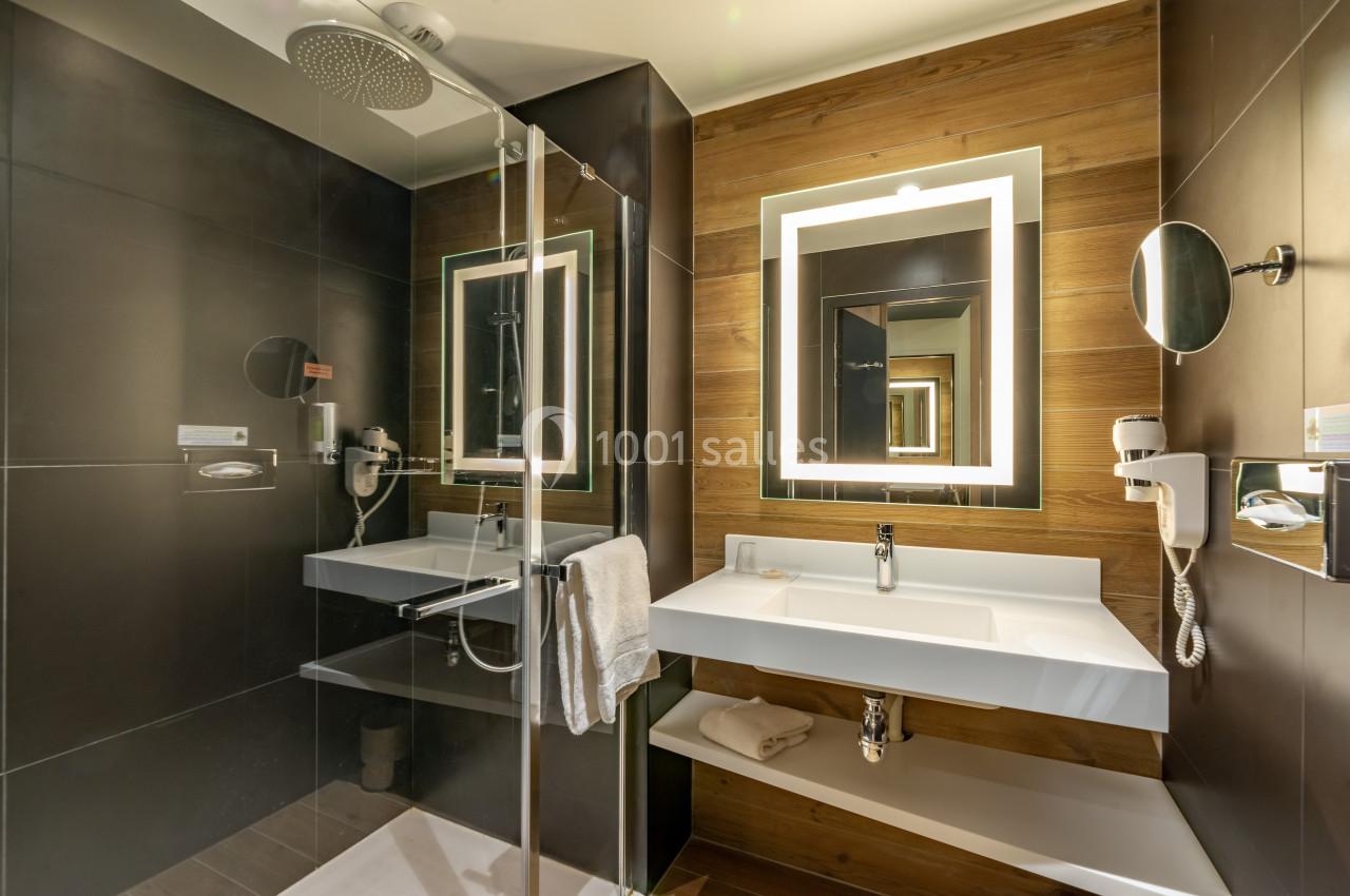 Salle de bain moderne avec douche à l'italienne, lavabo blanc, miroir éclairé et murs en bois et carrelage sombre.