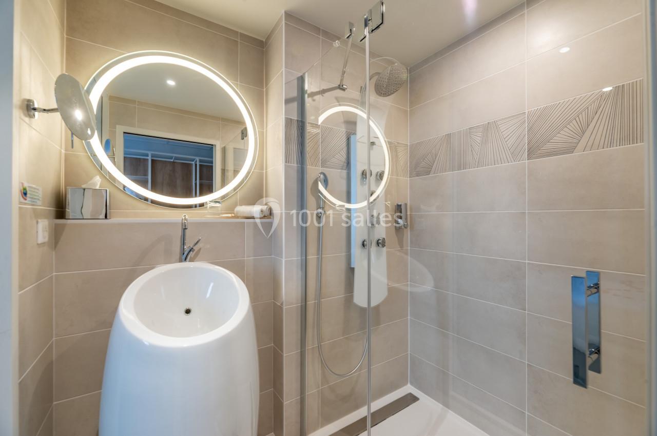 Salle de bain moderne avec douche à l'italienne, lavabo design et miroir rond éclairé.
