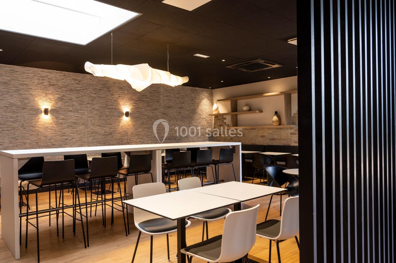 Salle moderne avec tables, chaises, éclairage design et murs texturés, ambiance lumineuse et épurée.