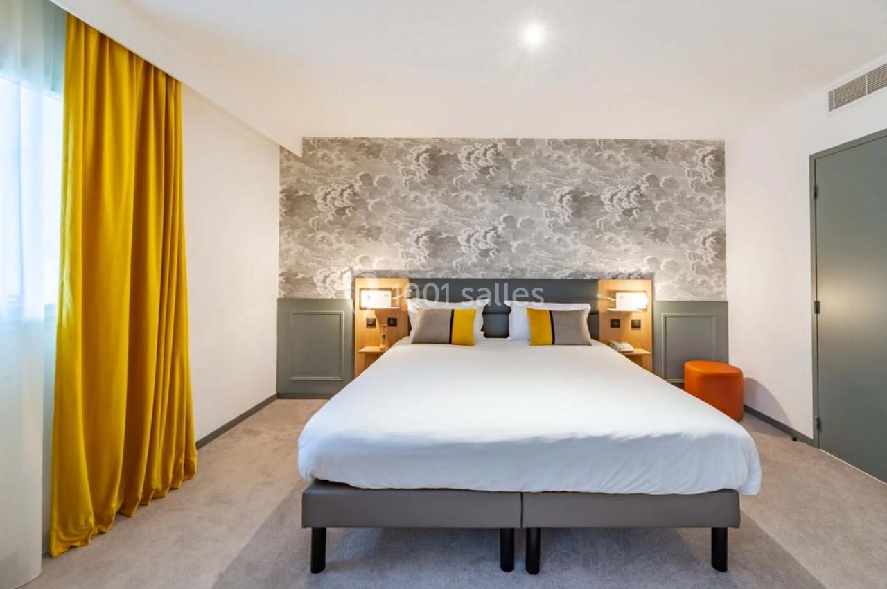 Chambre lumineuse avec un grand lit, des coussins jaunes, des rideaux assortis et un mur à motif nuageux.