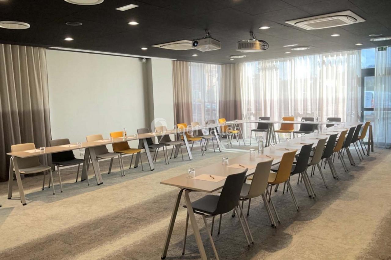 Salle de réunion lumineuse avec des tables et des chaises disposées en U, équipée de projecteurs au plafond.