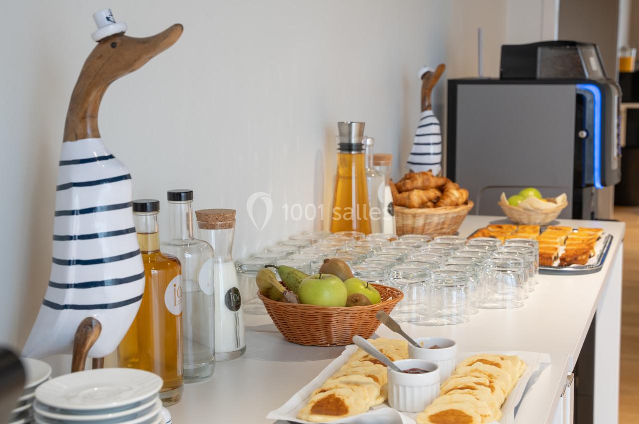 Table avec viennoiseries, fruits, jus, confitures et décorations en forme de canards marins en bois.