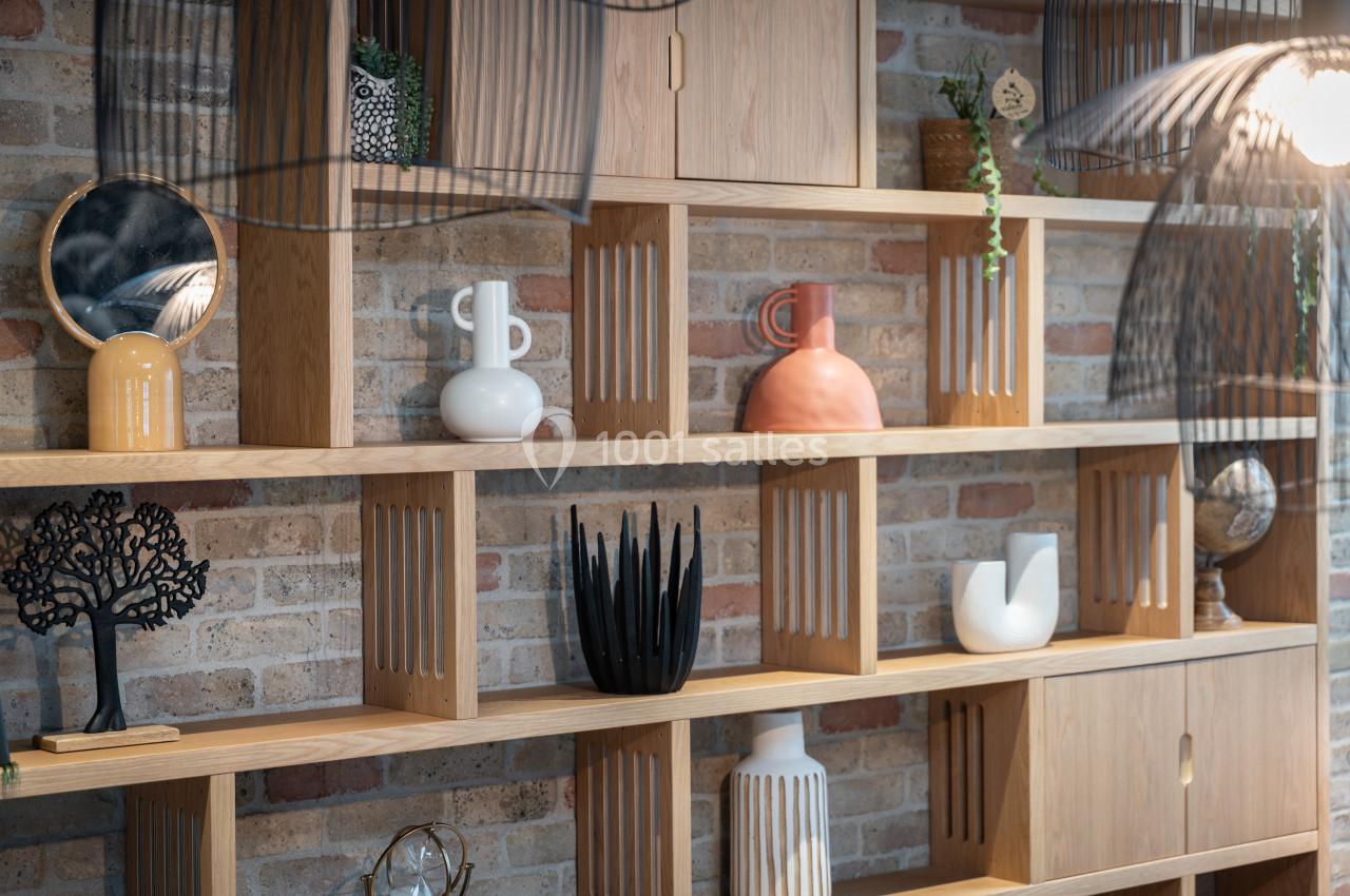 Étagère en bois clair contre un mur de briques, décorée d'objets variés comme vases, plantes et sculptures.