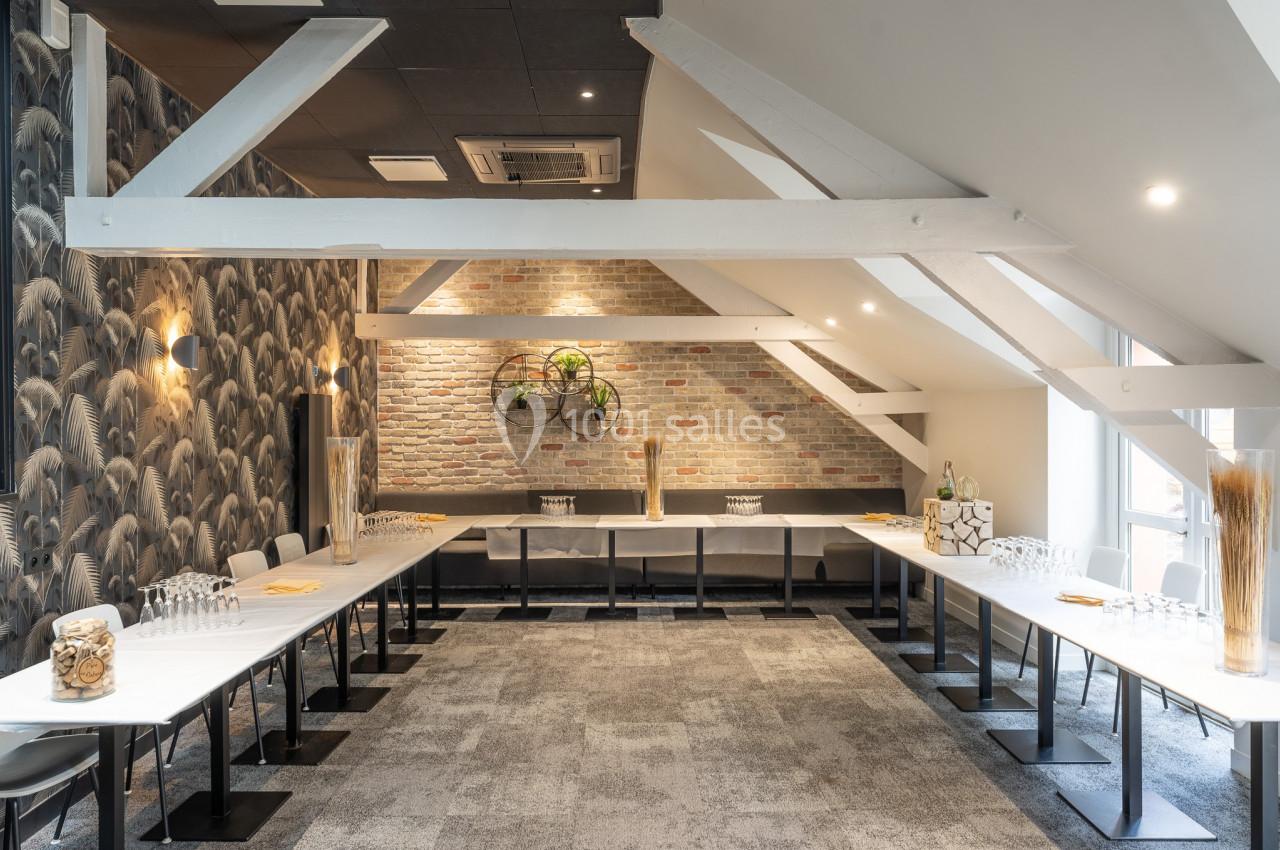 Salle de réunion lumineuse avec tables disposées en U, murs en briques et décorations modernes.