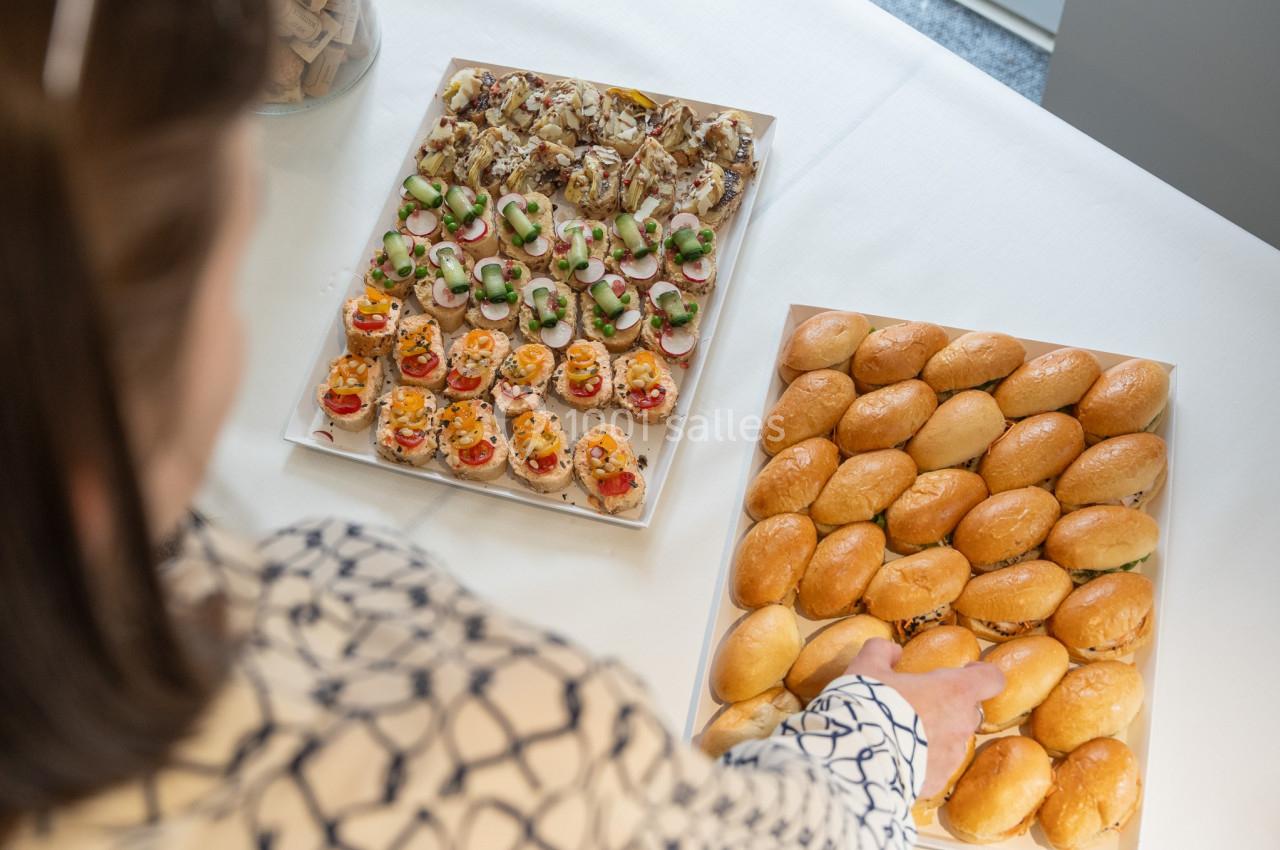 Une personne prend un petit pain sur une table garnie de plateaux de canapés variés et de pains.