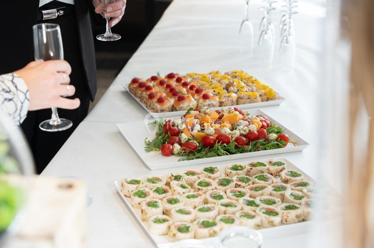 Plateaux de canapés variés disposés sur une table blanche, avec des personnes tenant des verres en arrière-plan.