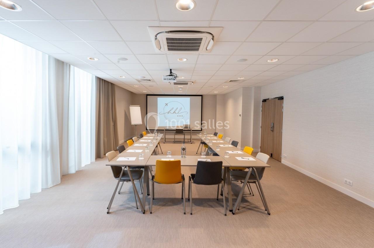 Salle de réunion lumineuse avec tables disposées en U, chaises colorées et écran de projection allumé.