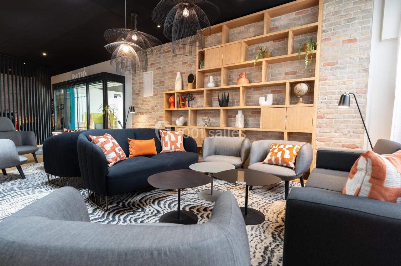 Espace salon moderne avec canapés, fauteuils, tables basses et étagères décoratives sur un mur en briques.