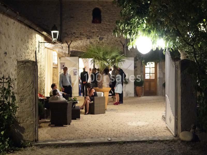 Personnes réunies dans une cour en soirée, éclairée par des lampes, entourée de murs en pierre et de végétation.