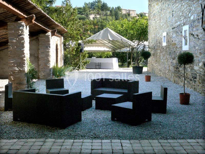 Mobilier de jardin noir disposé sur une terrasse en gravier, entourée de murs en pierre et de végétation.
