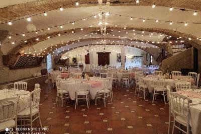 Salle de réception décorée avec des tables rondes dressées, des chaises blanches et des plantes entourant l'espace.