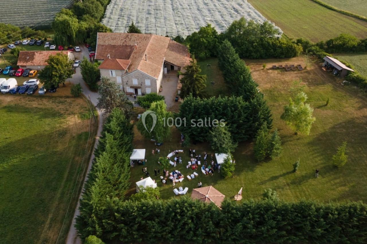 Vue aérienne d'une maison entourée de jardins, avec des invités réunis sous des tentes dans un cadre champêtre.