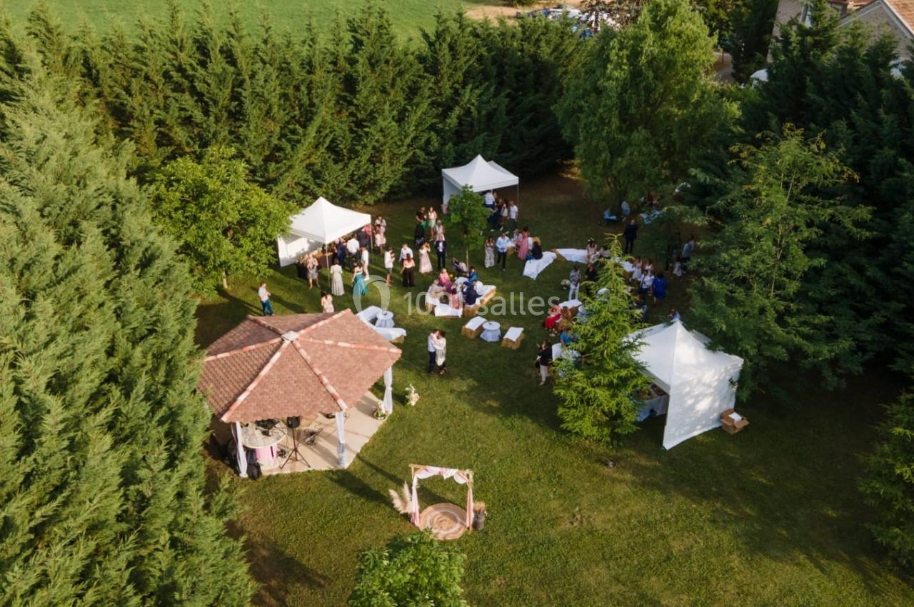Vue aérienne d'un événement en plein air avec des invités rassemblés sous des tentes blanches dans un cadre verdoyant.