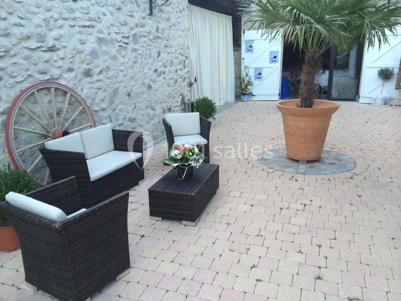 Salon de jardin en rotin avec coussins blancs, disposé sur une terrasse pavée près d'un palmier en pot.