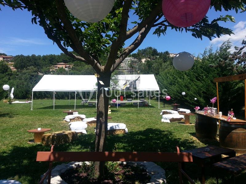 Espace extérieur aménagé pour un événement avec tente blanche, décorations suspendues et tables sur une pelouse.