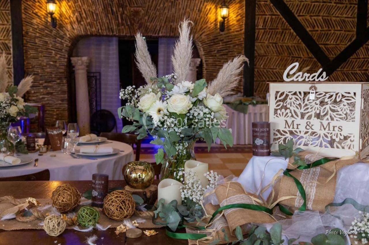 Décoration de table de mariage avec fleurs blanches, bougies, rubans et boîte pour cartes dans une salle rustique.