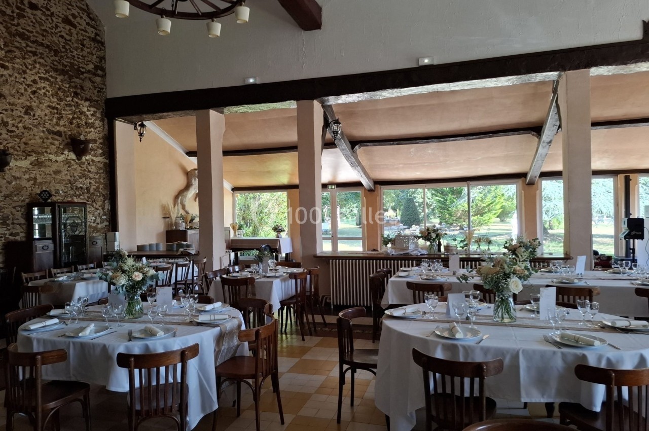 Salle de réception lumineuse avec tables rondes dressées, décorée de bouquets de fleurs et ouverte sur un jardin verdoyant.