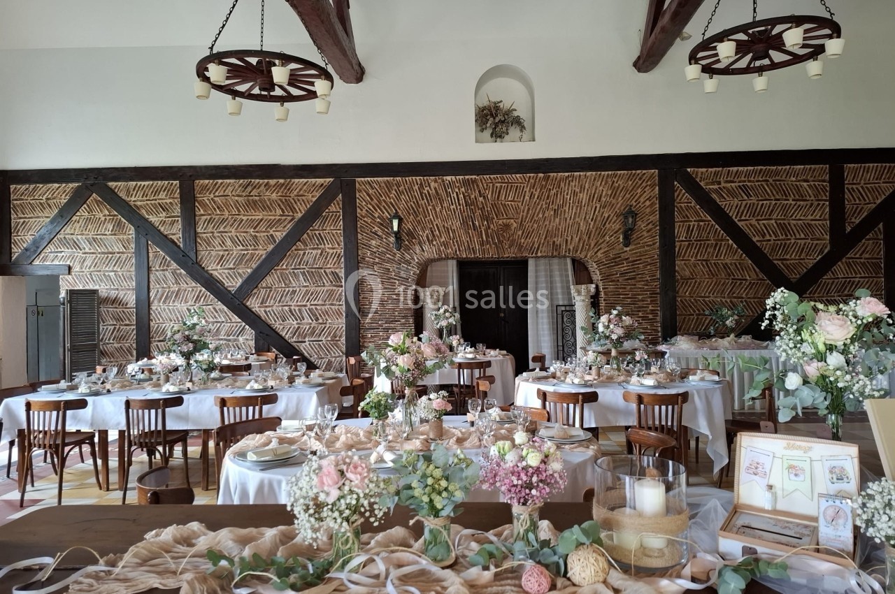 Salle de réception décorée pour un mariage avec tables dressées, fleurs, bougies et éléments rustiques en bois.