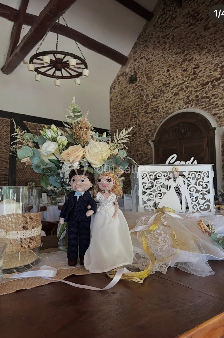 Figurines de mariés en laine posées sur une table décorée de fleurs, bougies et accessoires de mariage.