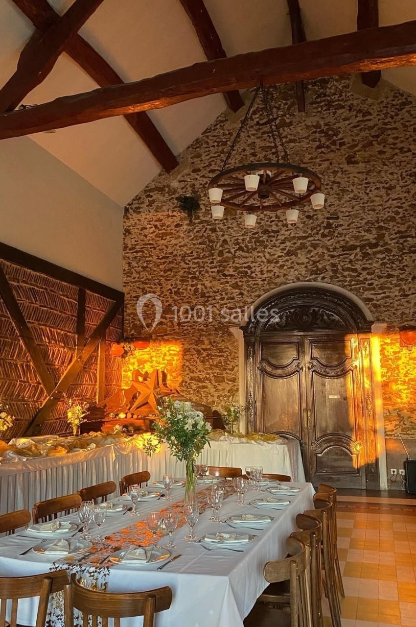 Salle de réception rustique avec murs en pierre, poutres apparentes, tables dressées et lumière chaude du coucher de soleil.