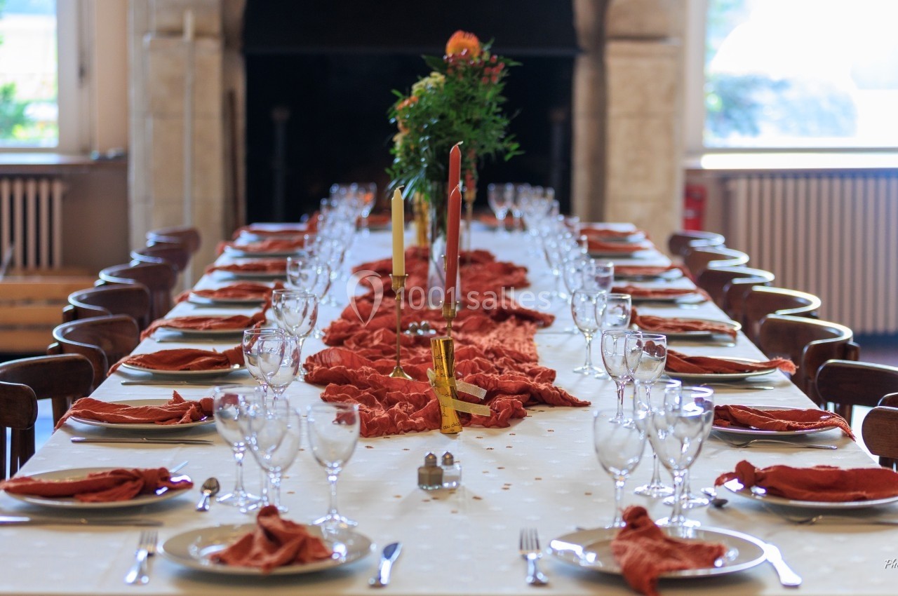 Grande table dressée avec nappes blanches, serviettes rouges, verres et couverts, décorée de bougies et fleurs au centre.