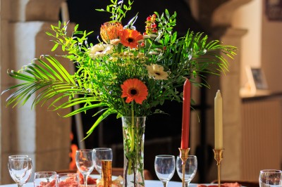 Grande table dressée avec nappes blanches, serviettes rouges, verres et couverts, décorée de bougies et fleurs au centre.