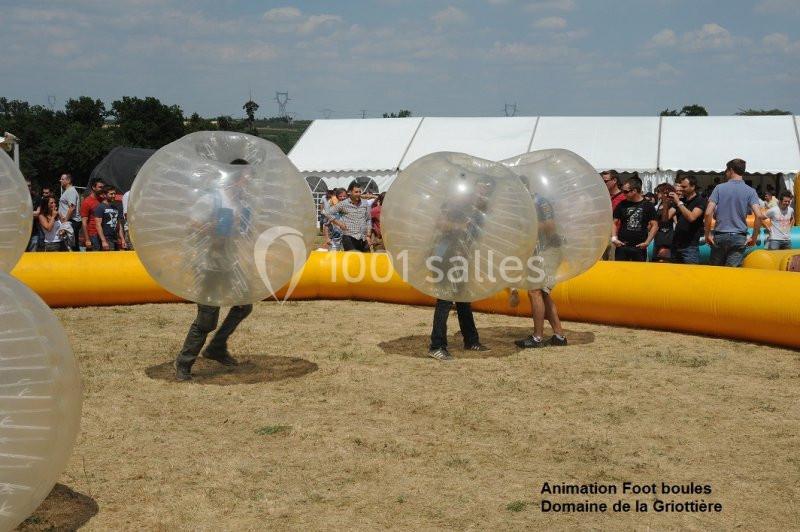 Des personnes jouent au bubble foot dans une aire délimitée, entourées de spectateurs et de tentes blanches.