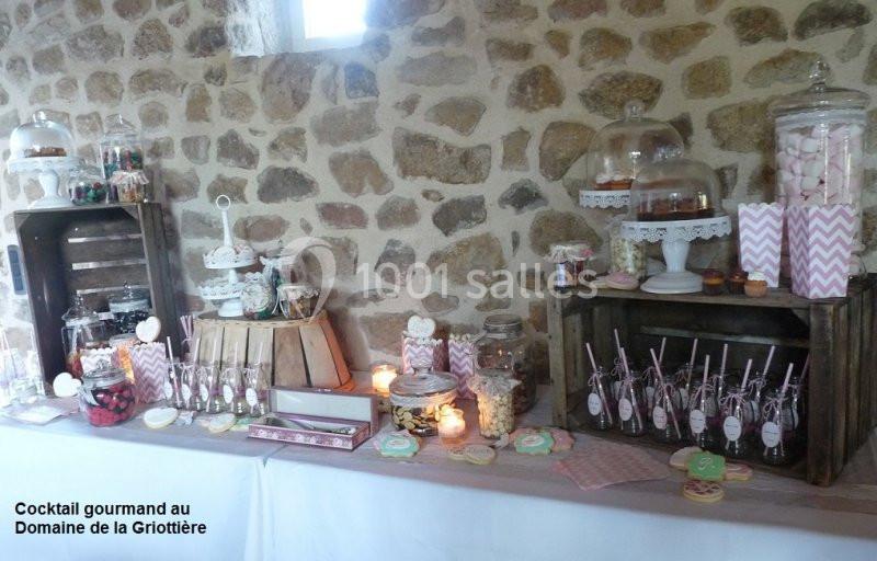 Table de buffet décorée avec des bonbonnières, friandises et desserts, disposée devant un mur en pierre.