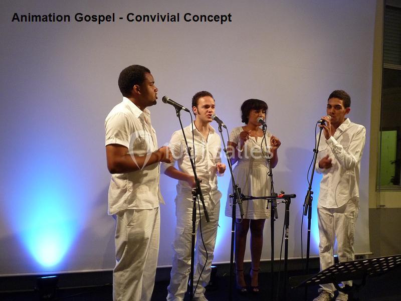 Quatre chanteurs en tenue blanche interprètent un morceau sur scène, avec des micros et un éclairage bleu en arrière-plan.