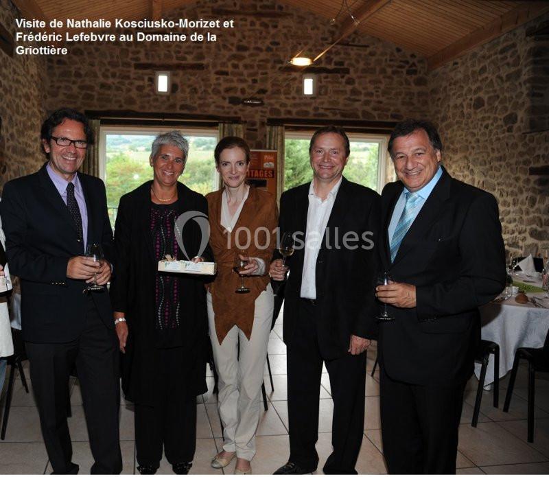 Cinq personnes posent debout dans une salle en pierre avec des tables dressées, tenant des verres à la main.