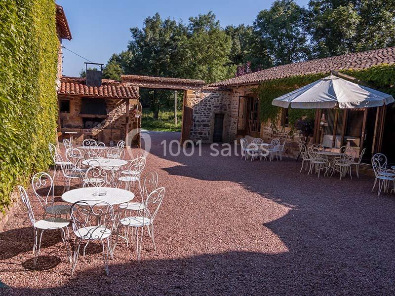 Cour extérieure avec tables et chaises en fer forgé, entourée de bâtiments en pierre et de végétation.