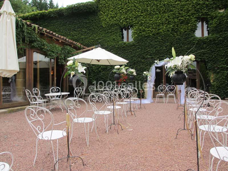 Cour extérieure avec chaises en fer forgé blanc, décor floral et mur recouvert de lierre, préparée pour un événement.