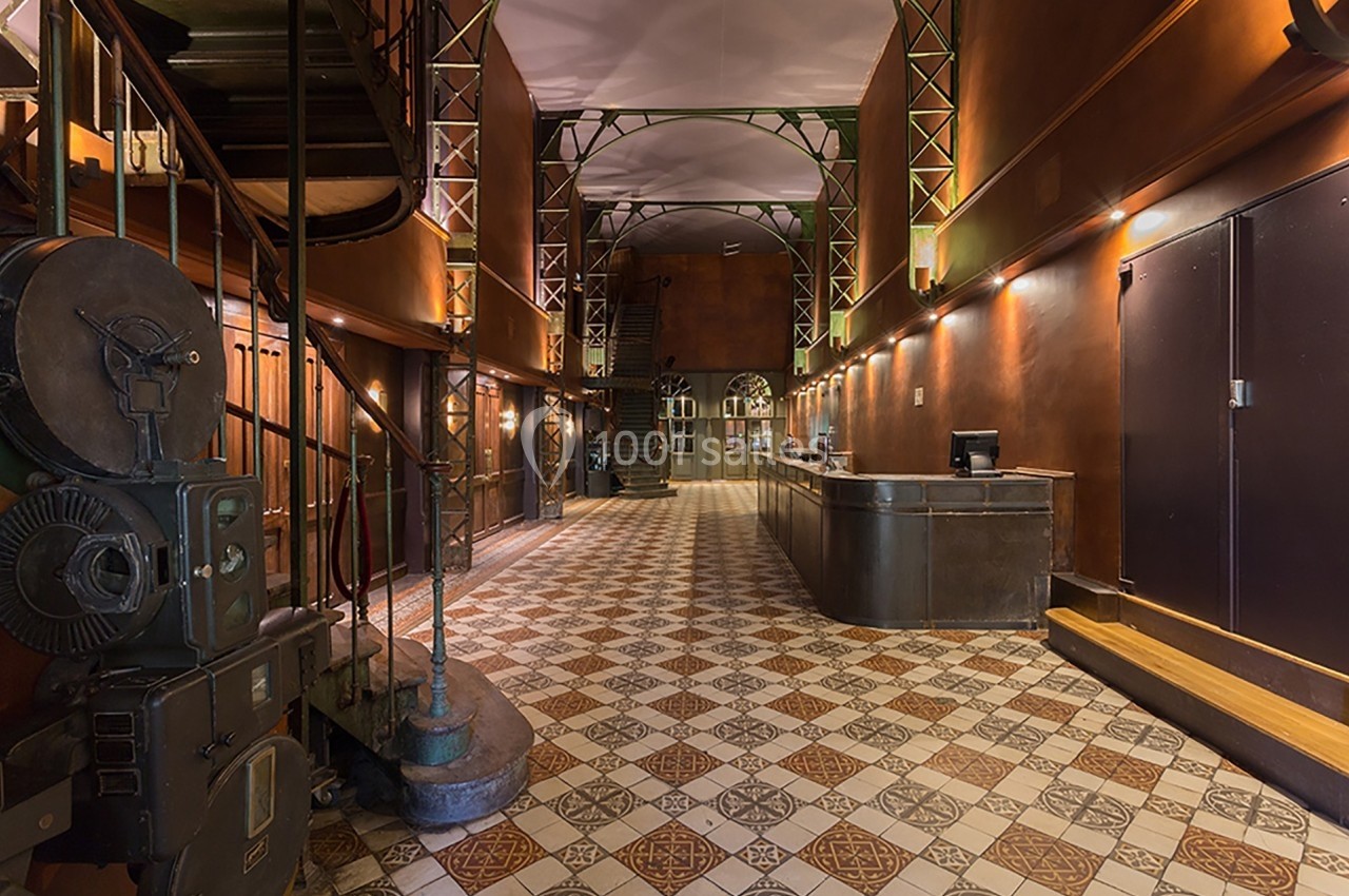 Intérieur d'un hall spacieux avec un sol carrelé, un escalier en colimaçon et un comptoir d'accueil en métal.