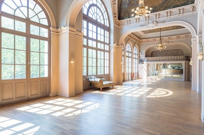 Hall spacieux avec sol en mosaïque, arches illuminées et tables décorées, éclairage chaleureux et ambiance élégante.