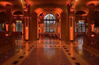 Hall spacieux avec sol en mosaïque, arches illuminées et tables décorées, éclairage chaleureux et ambiance élégante.