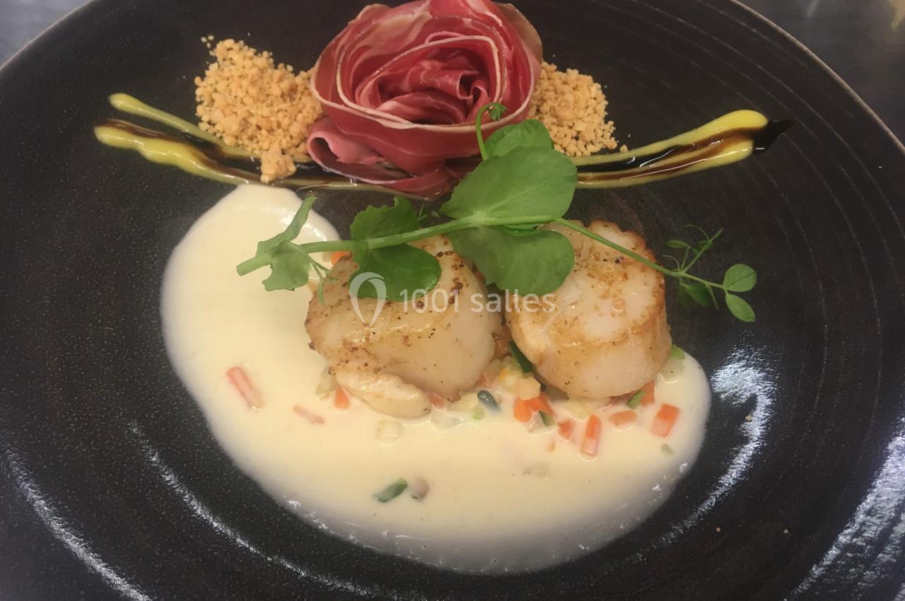 Assiette gastronomique avec noix de Saint-Jacques sur sauce crémeuse, garniture de légumes, chapelure et décoration florale.